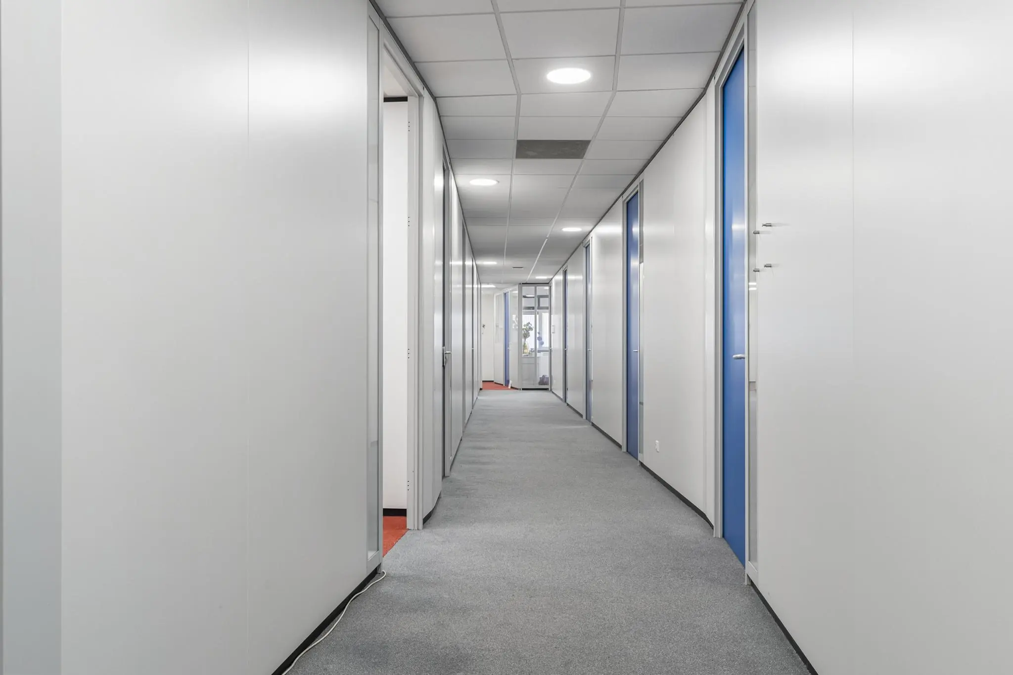 Lange, rechte gang in een kantoorgebouw aan de Huis-ter-Heideweg met deuren naar verschillende kamers en grijze vloerbedekking.